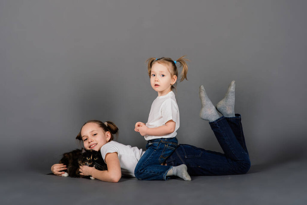 Two girls sisters hugging black cat in a studio - Photo, Image