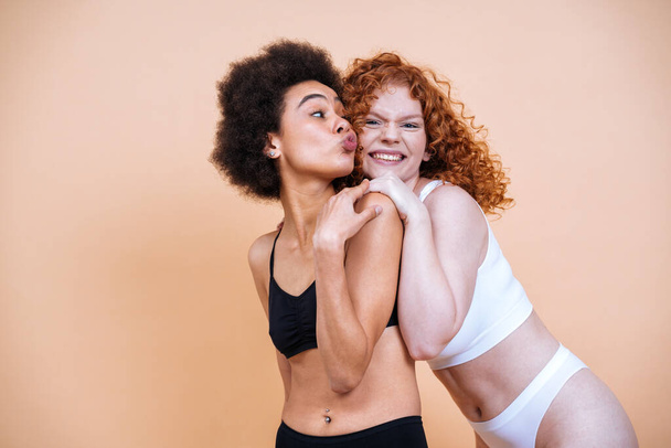beauty image of two young women with different skin and body posing in studio for a body positive photoshooting. Mixed female models in lingerie on colored backgrounds - Фото, изображение