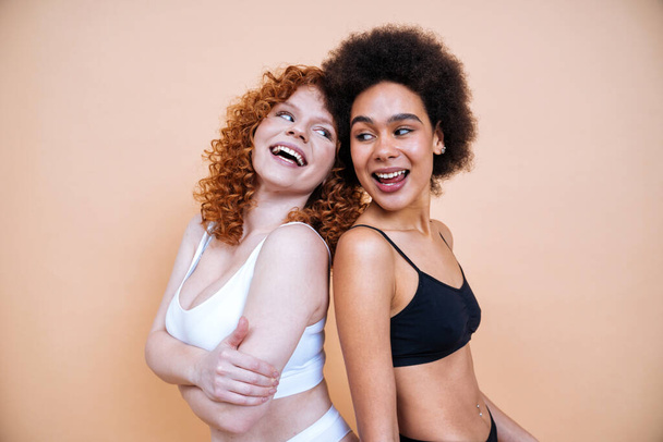 beauty image of two young women with different skin and body posing in studio for a body positive photoshooting. Mixed female models in lingerie on colored backgrounds - Foto, immagini