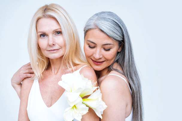 beauty image of two women with different age, skin and body posing in studio for a body positive photoshooting. Mixed female models in lingerie on colored backgrounds - 写真・画像