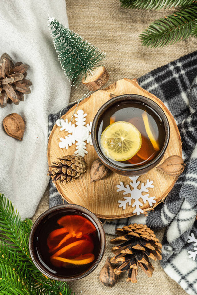 Hot black tea and lemon with winter decor. Cozy sweater, fir tree branches, nuts, snowflakes. Festive seasonal arrangement, good mood concept, rustic style, top view - Fotoğraf, Görsel