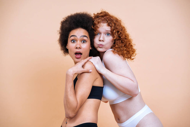 beauty image of two young women with different skin and body posing in studio for a body positive photoshooting. Mixed female models in lingerie on colored backgrounds - Valokuva, kuva