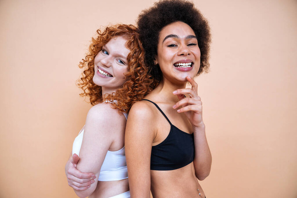 beauty image of two young women with different skin and body posing in studio for a body positive photoshooting. Mixed female models in lingerie on colored backgrounds - Zdjęcie, obraz