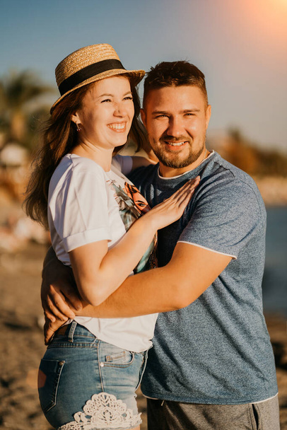  bright sun. a man and a woman in love squinting from the sun hug on the beach. - Φωτογραφία, εικόνα