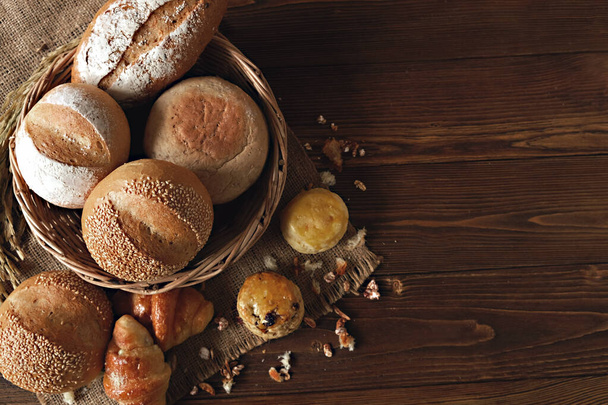 Un conjunto de pan de bollo en cesta y croissant en vista superior con trigo y saco en la mesa de madera. El espacio coppy a la derecha. - Foto, imagen