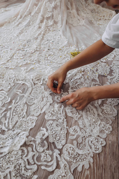 A professional atelier is putting needles on the beautiful white dress. She is perfecting her dress. The white dress is very long. There is a small box of yellow needles on the right side. - Photo, Image