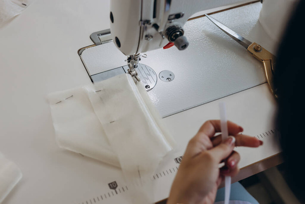 A creative master is making dress on the dressmaking table. There are scissors near her and equipment for work. She is working with fabric for wedding dress. - Photo, Image