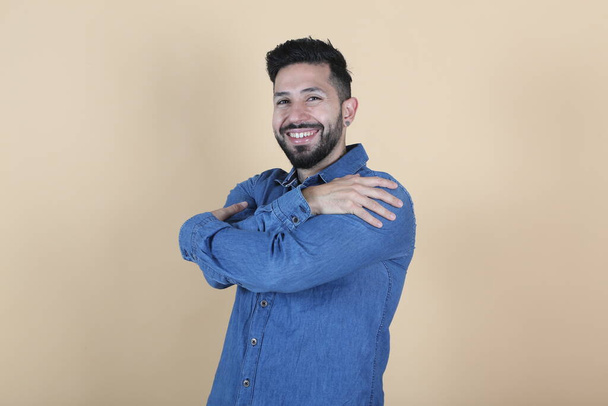 hispanic latino man smiles while hugging himself on yellow background - Foto, imagen