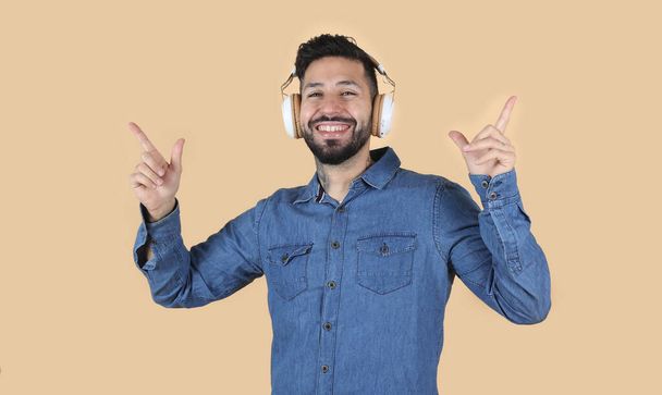 幸せなラテン系のヒスパニック男はヘッドフォンで音楽を聴き音楽的なジェスチャーをします - 写真・画像