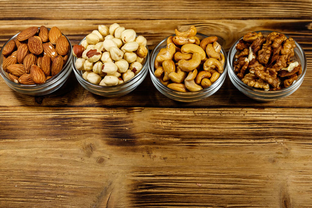 Assortment of nuts on wooden table. Almond, hazelnut, walnut and cashew in glass bowls. Top view, copy space. Healthy eating concept - Photo, Image