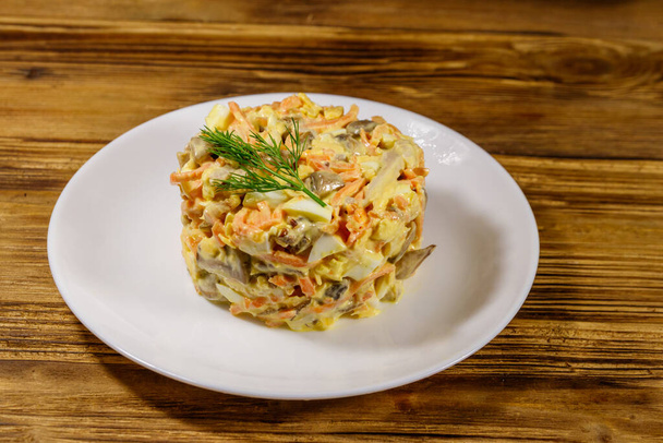 Lekkere salade met kipfilet, geroosterde champignons, wortelen, geraspte kaas, eieren en mayonaise op houten tafel - Foto, afbeelding