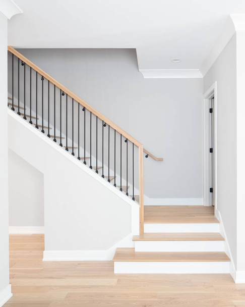 Лестница идет вверх с естественными деревянными ступенями и перилами, белые подъемы, и кованые железные веретена. - Фото, изображение