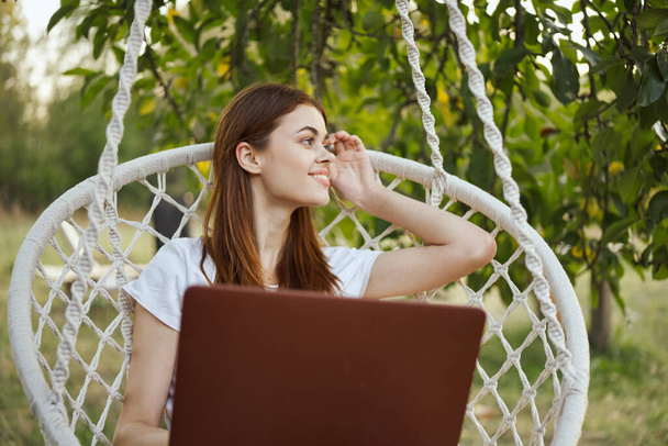 smiling woman outdoors in hammock with laptop technology - Fotó, kép