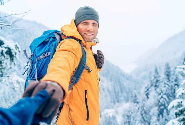 Happy smiling Man dressed bright orange softshell jacket with backpack hand in hand girlfriend point view on the winter mountains route. Active people in nature, help or follow me concept image. - Fotografie, Obrázek