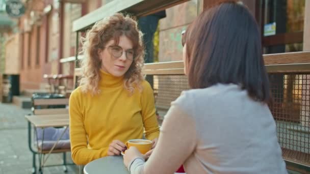Le donne parlano e bevono caffè a tavola per strada in una giornata autunnale - Filmati, video