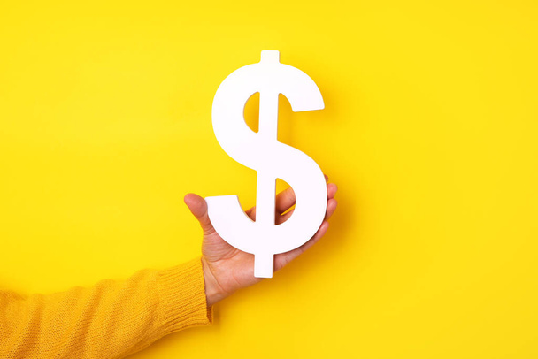 χέρι κρατώντας το σύμβολο του δολαρίου πάνω από κίτρινο φόντο, χρηματοοικονομική έννοια - Φωτογραφία, εικόνα