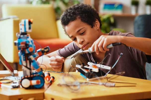 Kluger afrikanischer Junge bastelt zu Hause einen Roboter für den naturwissenschaftlichen Unterricht. Robotik und Bildung. - Foto, Bild