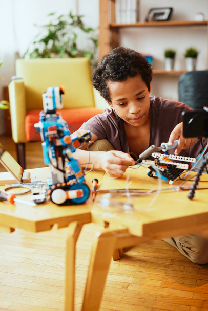 Omistautunut afrikkalainen koulupoika tekemässä robottia kotona tiedeluokkaa varten. Robotiikka koulussa - Valokuva, kuva