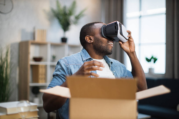 African man checking VR headset while opening parcel box - Photo, Image