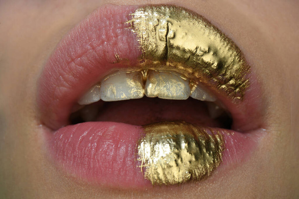 Gold lips. Gold paint from the mouth. Golden lips on woman open sensual mouth with make-up. Sensual and creative design for golden metallic. - Valokuva, kuva