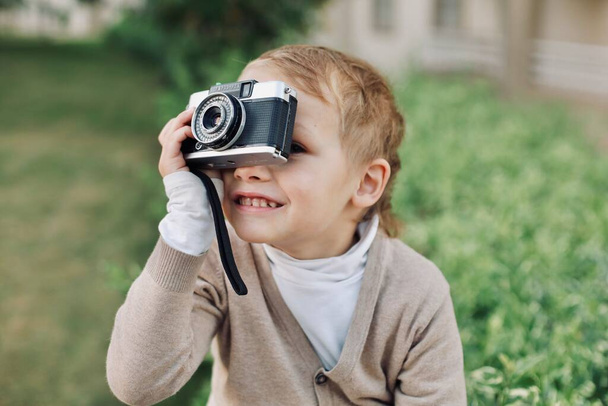 Μικρό γοητευτικό αγοράκι που κοιτάζει αν και σκόπευτρο του φιλμ αναλογική vintage φωτογραφική μηχανή και χαμόγελο, τα παιδιά και τα παλιά πράγματα - Φωτογραφία, εικόνα