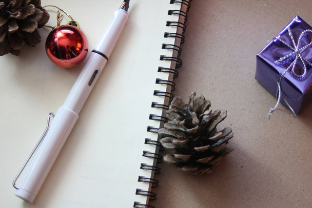 Üres füzet, toll, szárított fenyőtoboz, karácsonyi labda és egy kis ajándékdoboz. Helyszín az újrahasznosított papíron - Fotó, kép