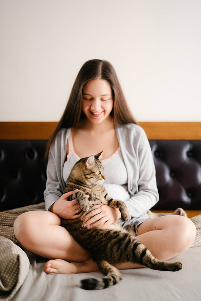 Pregnant woman sitting on bed with cat - Photo, Image