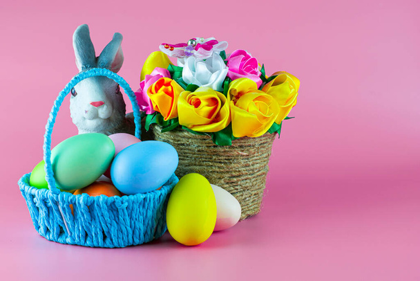 conejito de Pascua y huevos de Pascua pintados en una canasta junto a una canasta de flores sobre un fondo rosa. copyscape. Foto de alta calidad - Foto, Imagen