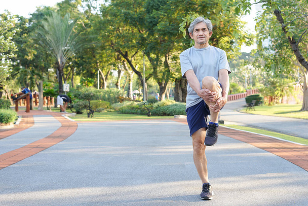 un hombre mayor calentando antes de correr en el parque, concepto de ejercicio de calentamiento prevenir lesiones en personas mayores - Foto, imagen