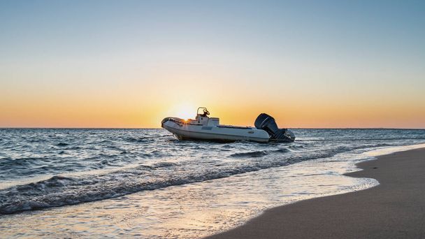 モーターボートは波に揺られている。砂浜の泡だ。明け方の空はオレンジで強調されている。昇る太陽の光が輝いている。エジプトだ。紅海. - 写真・画像