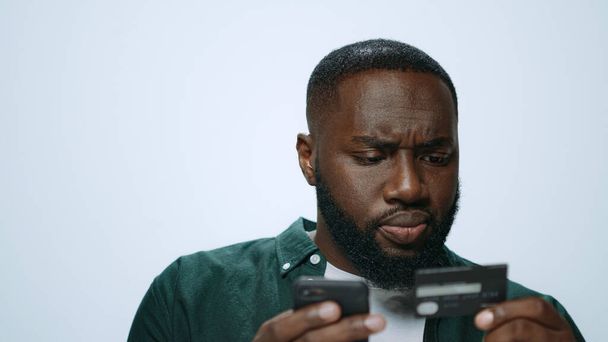 Портрет серьезного африканца, делающего покупки онлайн на смартфоне в студии - Фото, изображение