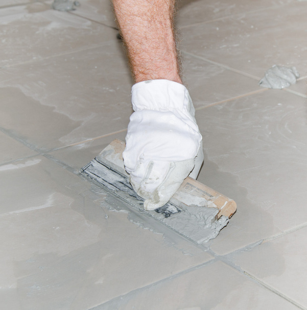 Tiler filling up joints with a rubber squeegee - Foto, Imagen
