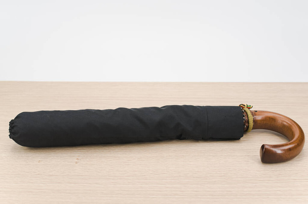 black foldable umbrella with solid wood handle on a wooden surface with copy space - Zdjęcie, obraz