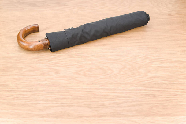 black foldable umbrella with solid wood handle on a wooden surface with copy space - Fotoğraf, Görsel