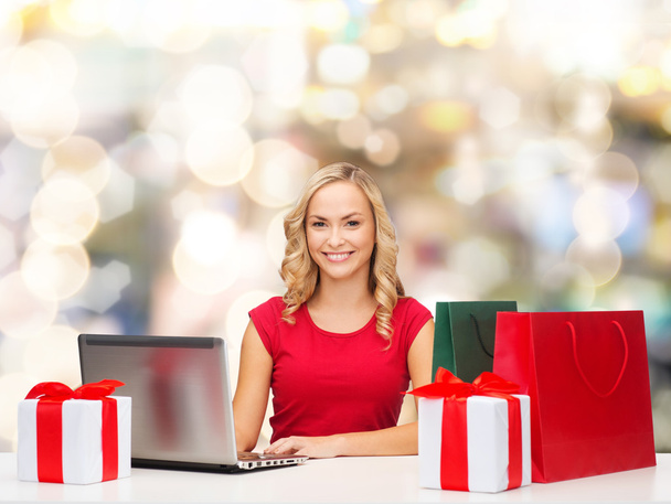 mosolygó nő piros póló, ajándékok és a laptop - Fotó, kép