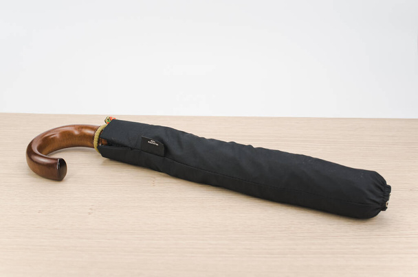 black foldable umbrella with solid wood handle on a wooden surface with copy space - Foto, imagen