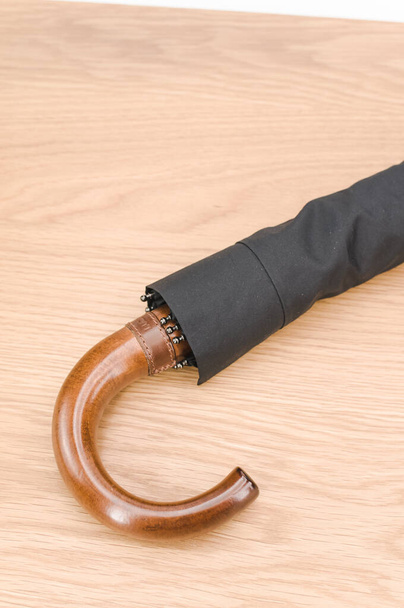 black foldable umbrella with solid wood handle on a wooden surface with copy space - Photo, image