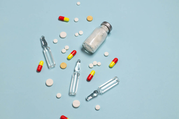 Vaccin en spuit, diverse farmaceutische pillen, tabletten en capsules op blauwe achtergrond. Gezondheidszorg en medisch concept. - Foto, afbeelding