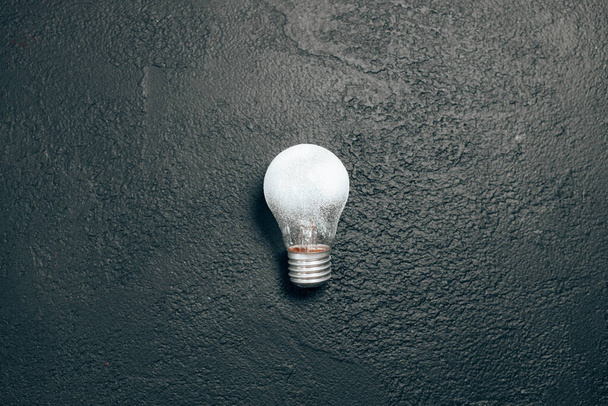 Идея одной белой лампочки на фоне тёмной гранж-доски. Творческое вдохновение, концепция идей планирования. Плоская кладка, вид сверху, копировальное пространство - Фото, изображение