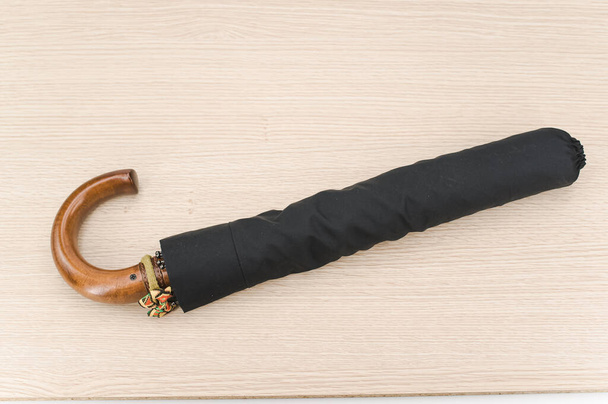black foldable umbrella with solid wood handle on a wooden surface with copy space - Foto, imagen