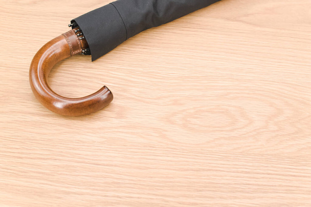 black foldable umbrella with solid wood handle on a wooden surface with copy space - Photo, Image