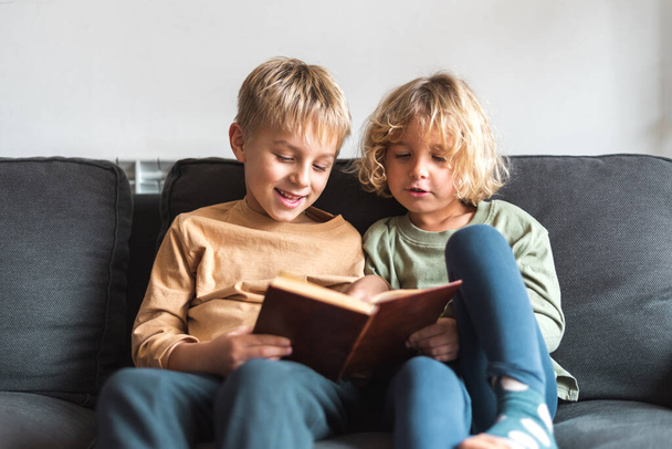 Adorable little siblings reading book on couch - Fotoğraf, Görsel