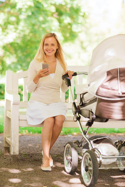 happy mother with smartphone and stroller in park - Photo, image