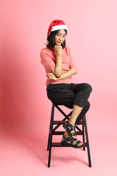 Портрет девушки смешанной расы в шляпе Сант Клауса, сидящей на розовом фоне. - Фото, изображение