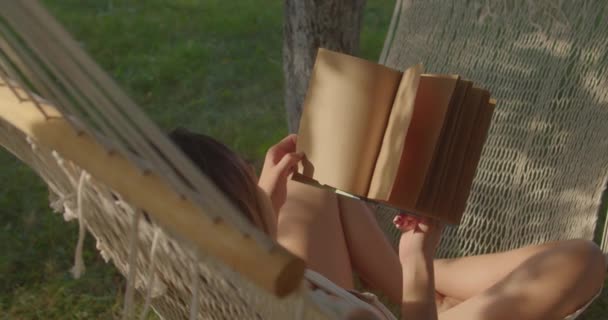 Teenage dívka má odpočinek v tkané houpací sítě čtení knihy - Záběry, video