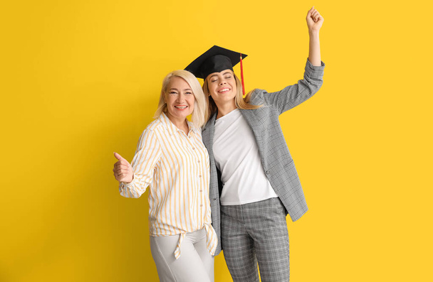Ευτυχισμένη φοιτήτρια αποφοίτησης με τη μητέρα της σε έγχρωμο φόντο - Φωτογραφία, εικόνα