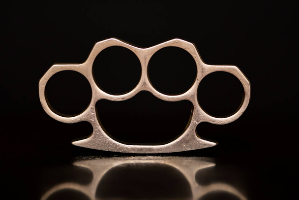 Steel brass knuckles on a black background with reflections. Concept: hooligan fight, fighting without rules, street banditry, injuries. - Photo, Image