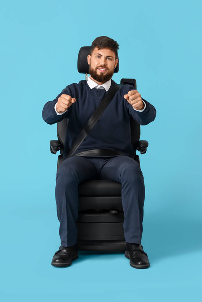 Όμορφος άντρας με φανταστικό τιμόνι σε κάθισμα αυτοκινήτου σε μπλε φόντο - Φωτογραφία, εικόνα