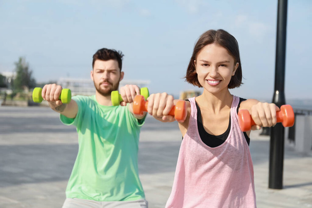 Sporty young woman and her husband training with dumbbells outdoors - Photo, Image