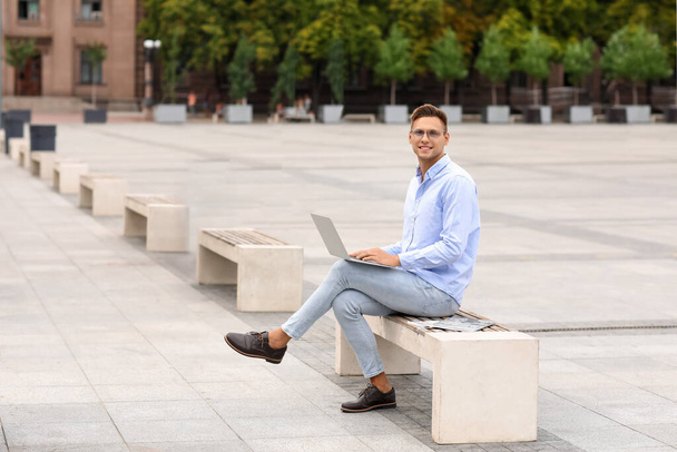 Handsome young businessman using laptop on city square - Fotoğraf, Görsel